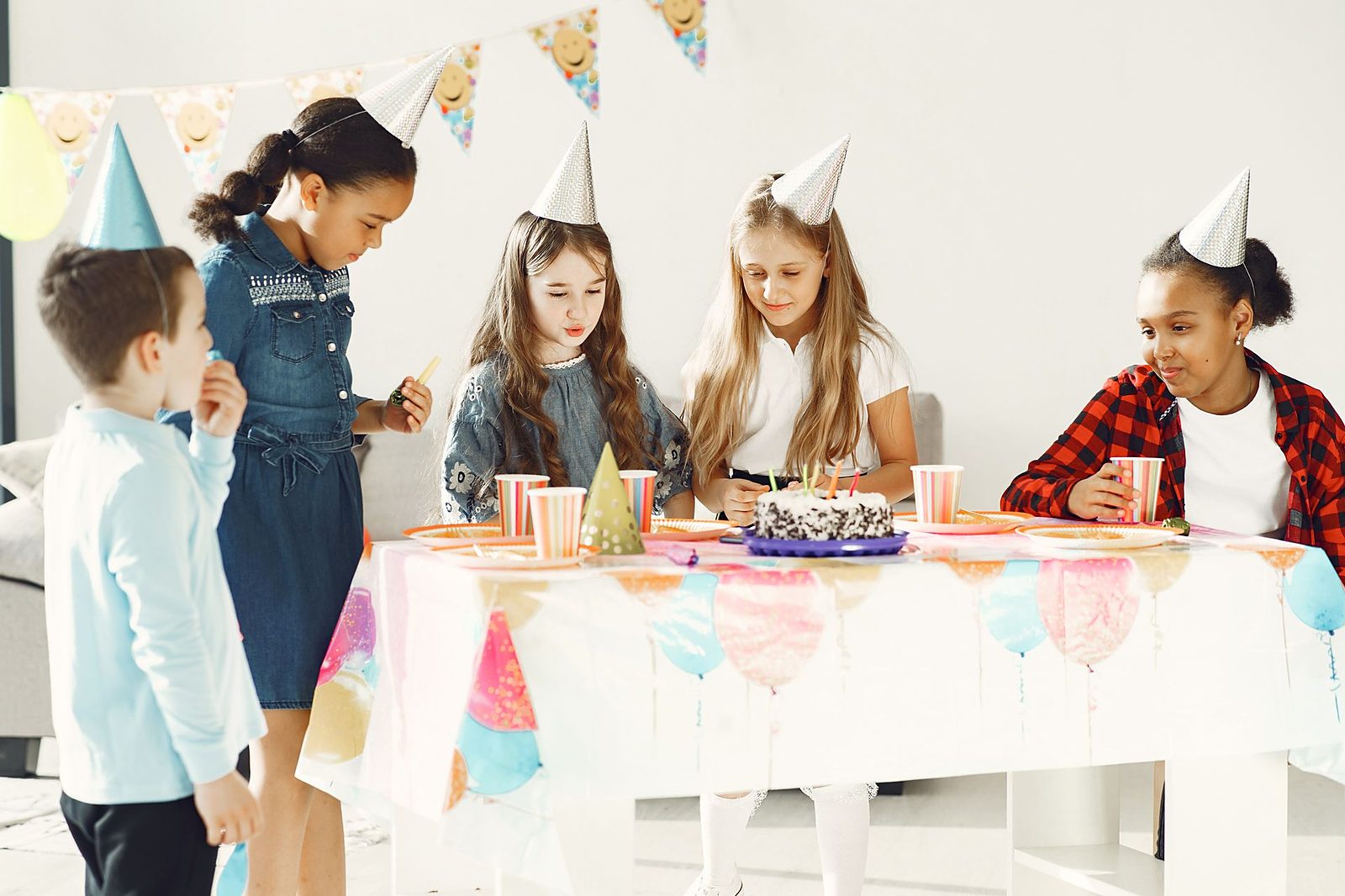 Children in party hats around a birthday table with cake and bunting