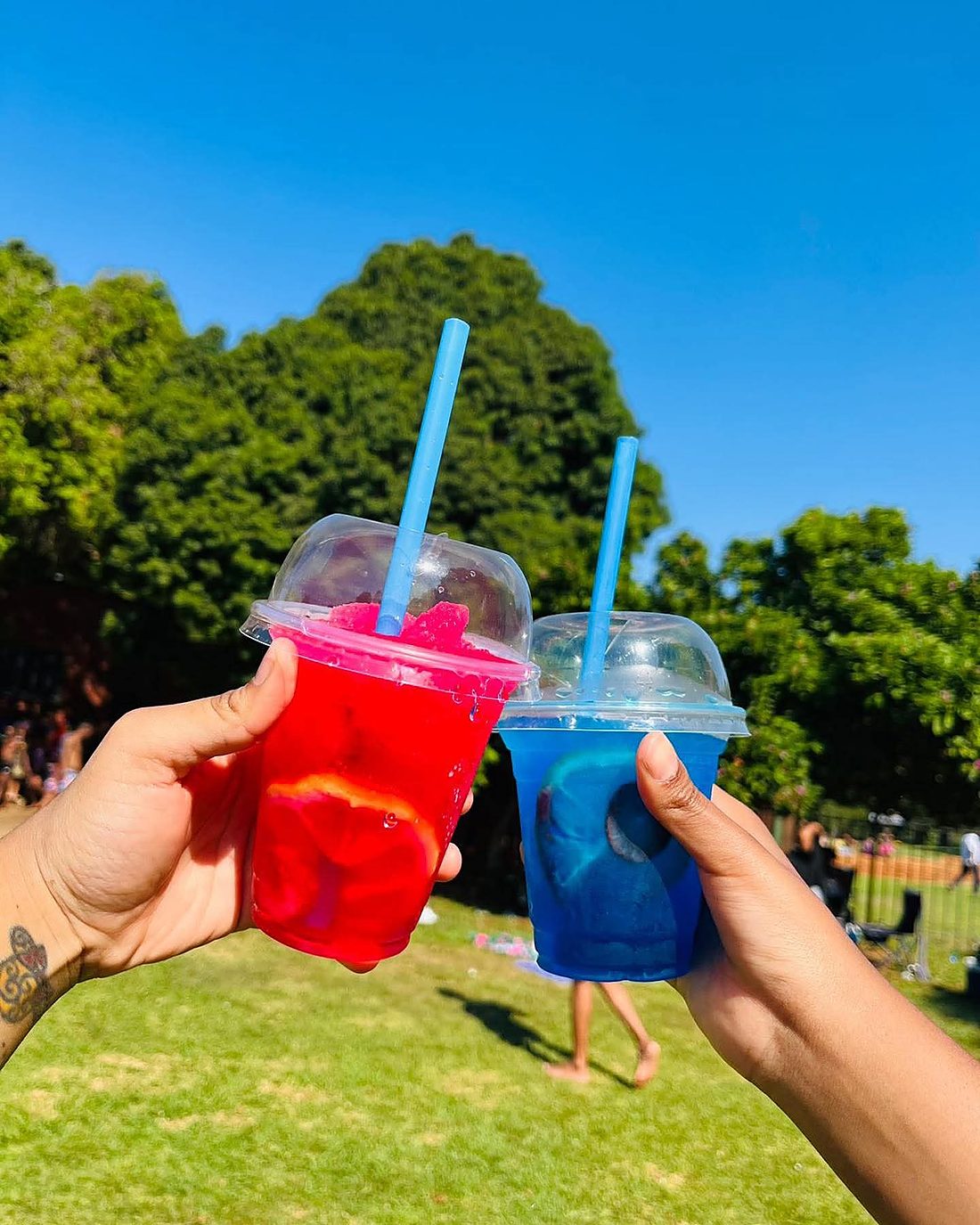 Two hands toasting with red and blue slush cups in the sunshine